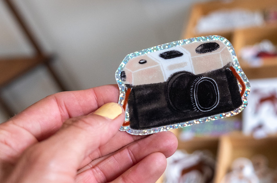 Hand holding a holographic sticker of a vintage black-and-white film camera.