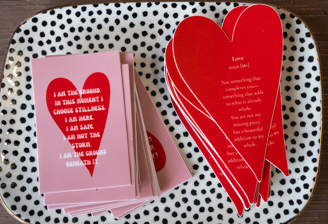 Stack of pink heart-shaped affirmation stickers reading “I am the ground” displayed on a dotted ceramic tray.