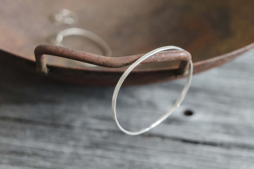 Close-up of a handcrafted hammered silver bracelet hanging on a rustic metal bowl handle, showcasing its subtle texture.